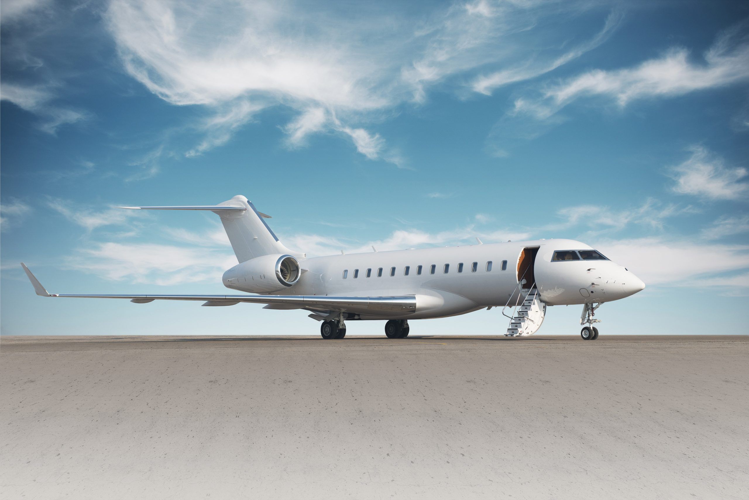 A Bombardier Global private jet with its airstair down on the apron under a blue sky