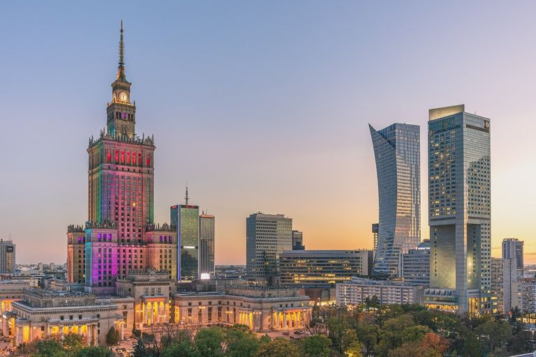 The illuminated Palace of Culture and Science beside Warsaw's modern skyline at dusk
