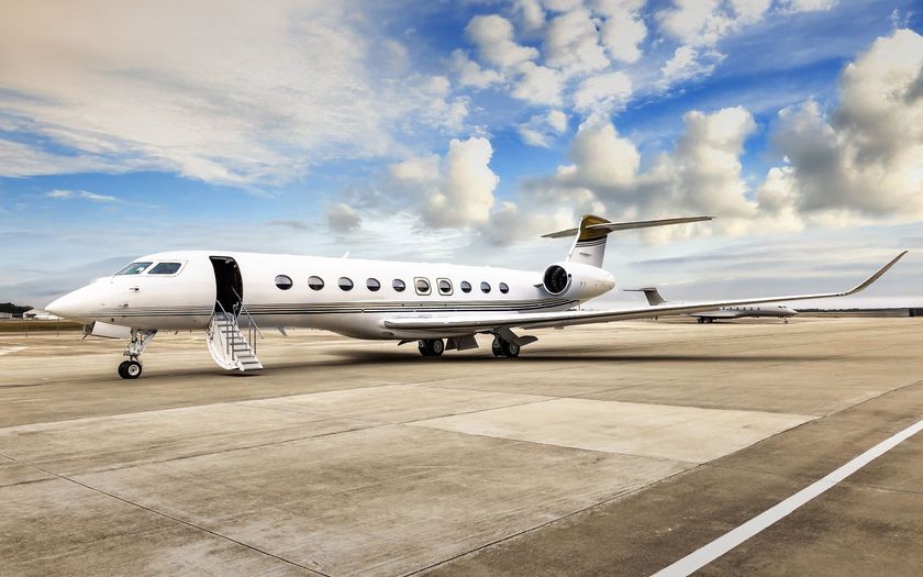 White Gulfstream G700 private jet with gold pinstripes parked on an apron, airstairs lowered