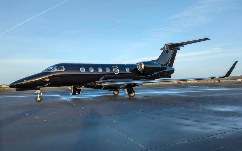 Black Embraer Phenom 300E private jet parked on an apron under a blue sky