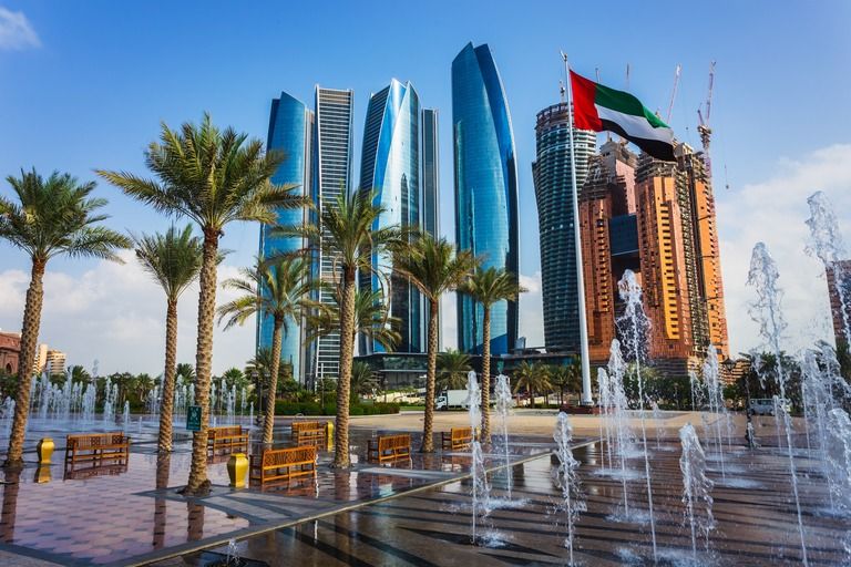 Etihad Towers skyline in Abu Dhabi framed by palm trees and fountains, with the UAE flag flying