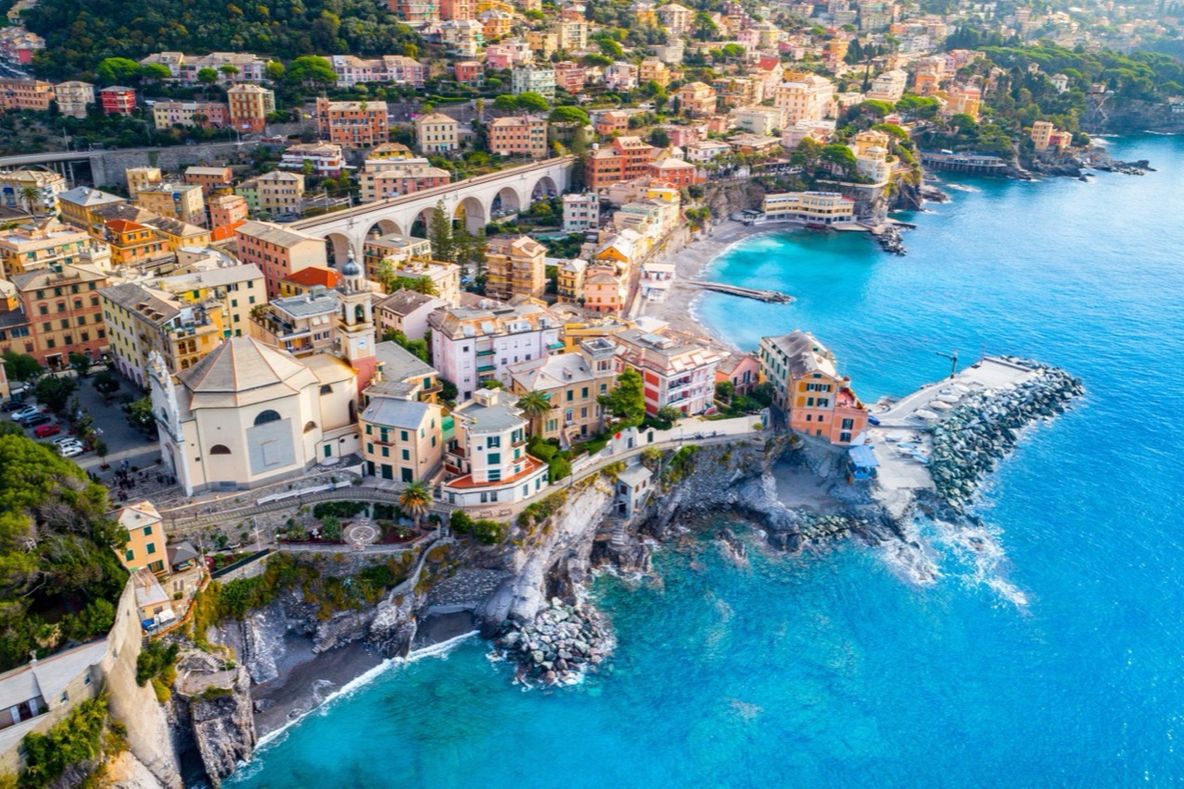 Veduta aerea di una cittadina costiera mediterranea con case pastello sopra una baia turchese