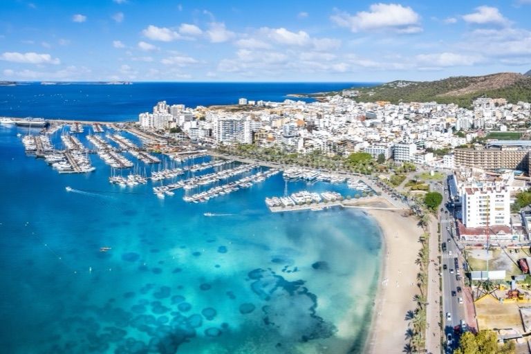 Veduta aerea di un porto turistico di Ibiza con yacht accanto a una baia turchese e una spiaggia di sabbia