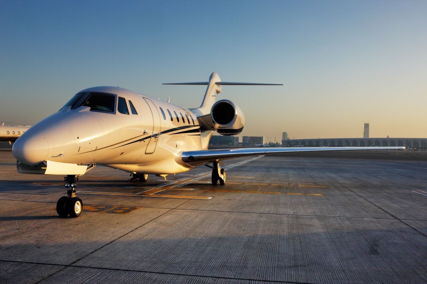 Jet privato in sosta sul piazzale al tramonto con un terminal aeroportuale sullo sfondo